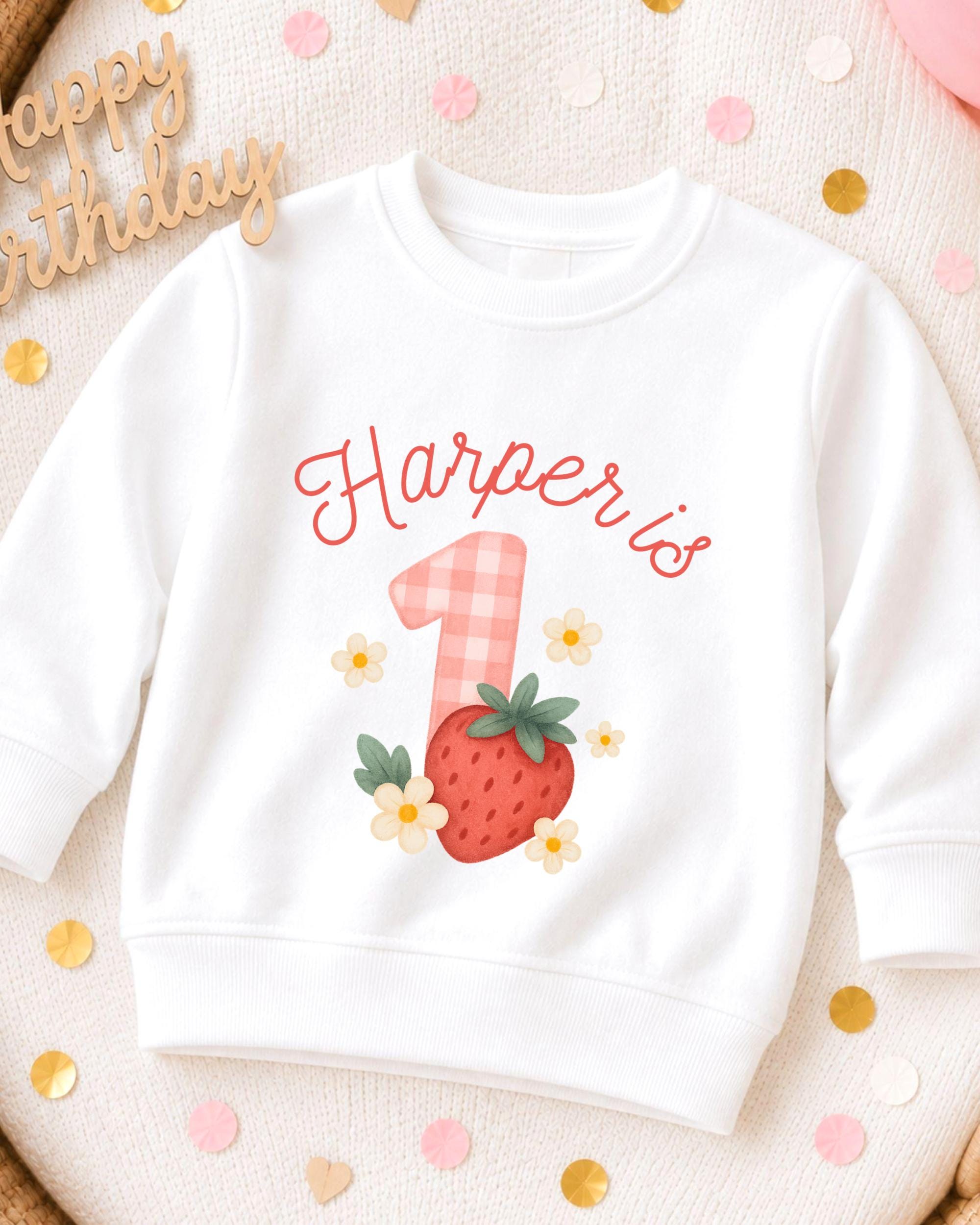 A white sweatshirt with a personalized design on it, featuring a strawberry and flowers, and the name "Harper's" written on it.