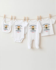 A row of four white baby clothes with the text "Born to play tennis" printed on them, hanging on a clothesline.