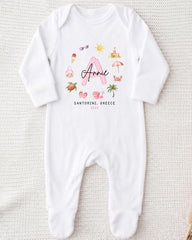 A white onesie with a personalized design featuring a pink letter "A" surrounded by various summer-themed illustrations, such as a beach, sunglasses, and a palm tree.
