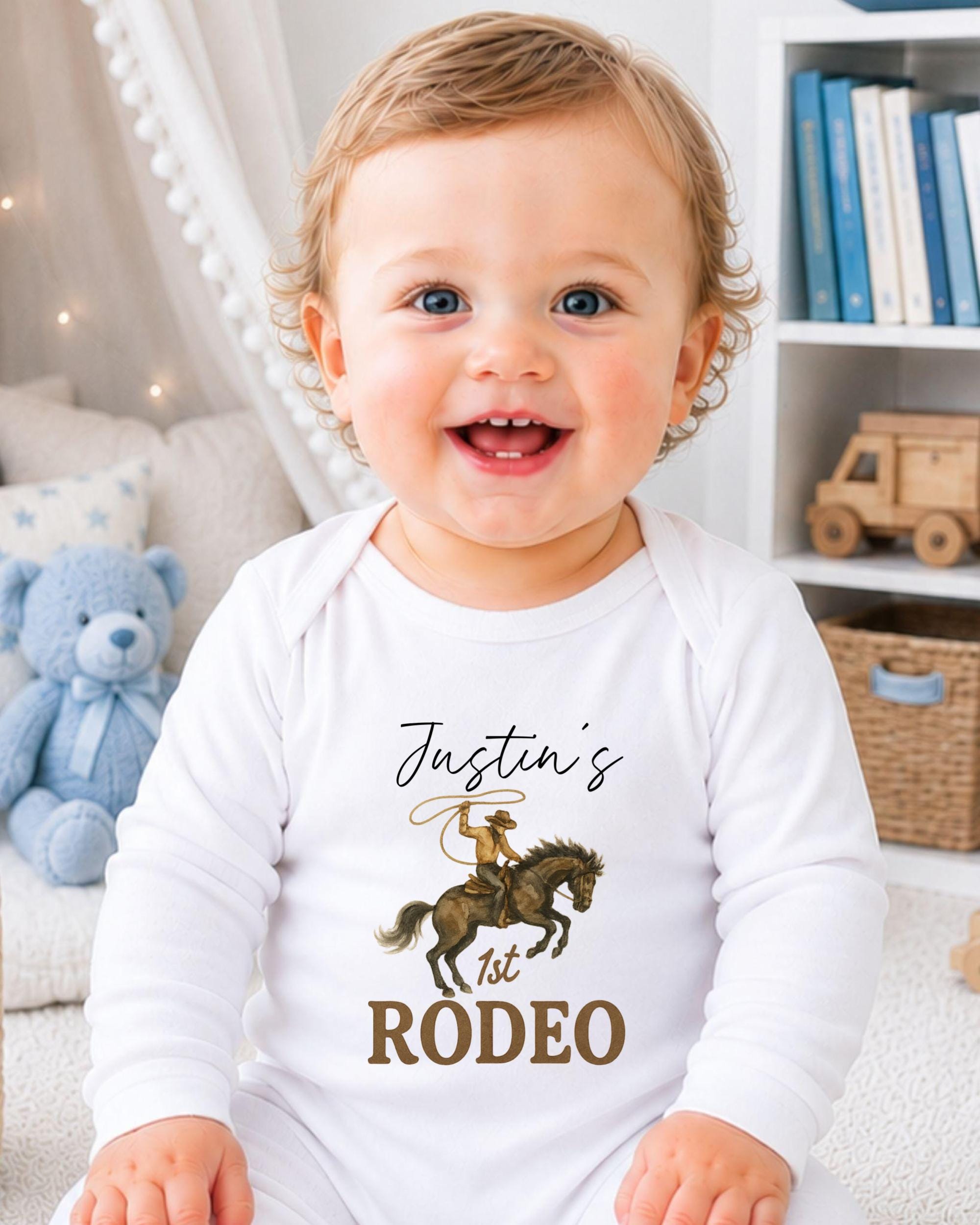 A smiling baby boy wearing a white onesie with a cowboy graphic and the text " Justin's 1st Rodeo" printed on it.