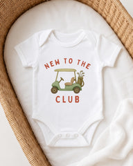 A white baby onesie with a golf cart graphic and the text "NEW TO THE CLUB" printed on it.