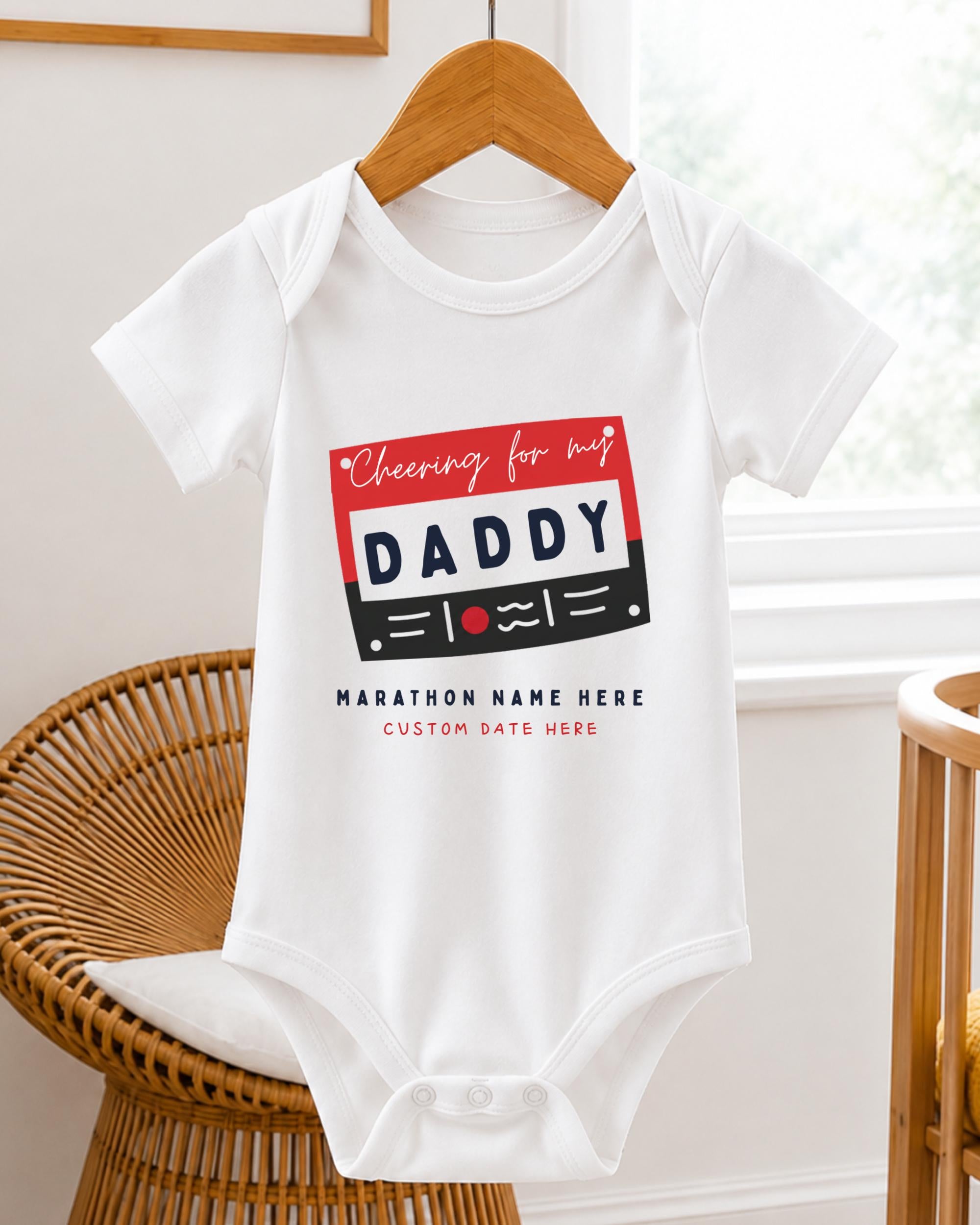 A white baby onesie with a graphic design on it, hanging on a wooden hanger.