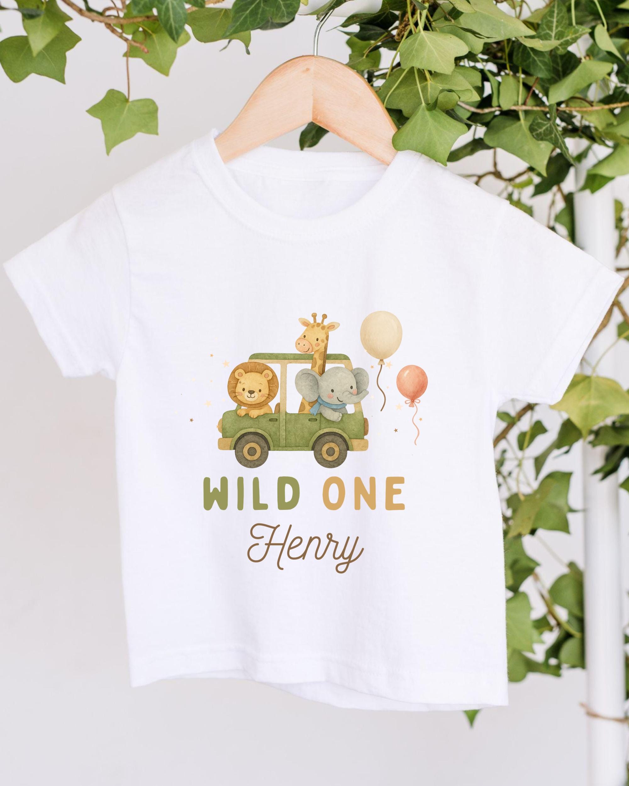 A white t-shirt with a graphic design featuring a safari scene with a lion, giraffe, and elephant, along with a balloon and the text "WILD ONE Henry".