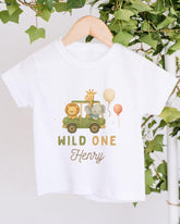A white t-shirt with a graphic design featuring a safari birthday scene with a lion, giraffe, and elephant, along with a balloon and the text "WILD ONE Henry".
