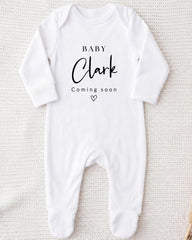 A white onesie with the text "BABY Clark Coming soon" printed on it.