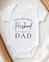 A white onesie with text printed on it, placed on a white surface.