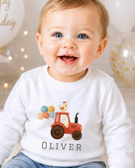 A smiling baby boy wearing a white shirt with a tractor and balloons printed on it.
