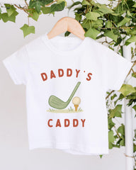 A white t-shirt with a graphic design featuring a golf club and ball, along with the text "DADDY'S CADDY".