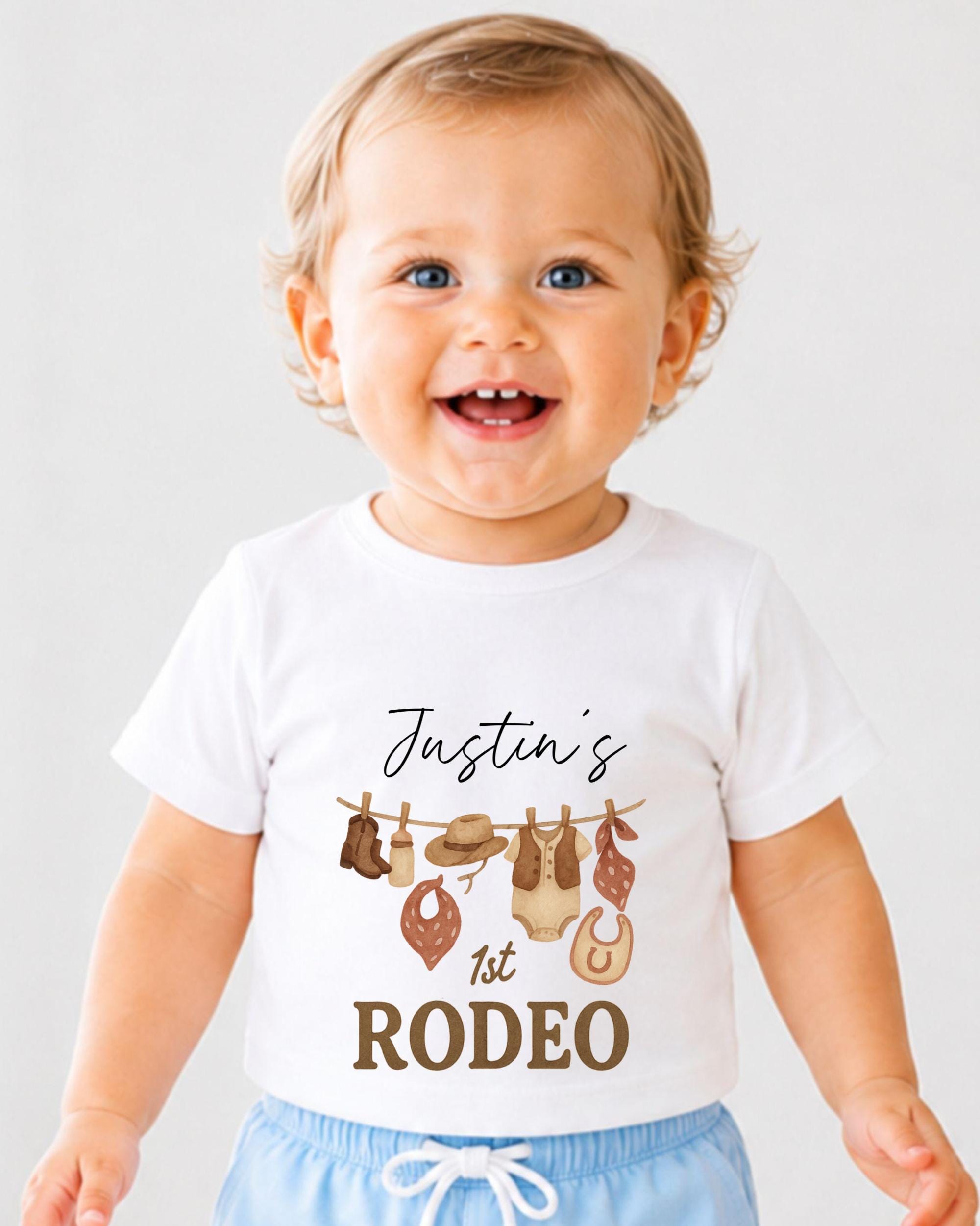 A smiling baby boy wearing a white t-shirt with a graphic design and text printed on it.
