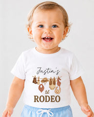A smiling baby boy wearing a white t-shirt with a graphic design and text printed on it.