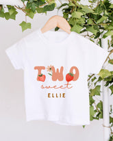 A white t-shirt with the text "TWO sweet Ellie" printed on it, along with illustrations of strawberries and leaves.