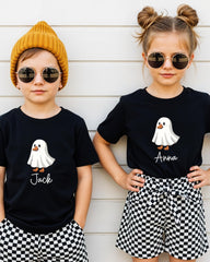 Two children wearing black t-shirts with a ghost graphic and the name "Jack" printed on them, along with round sunglasses and a yellow beanie.