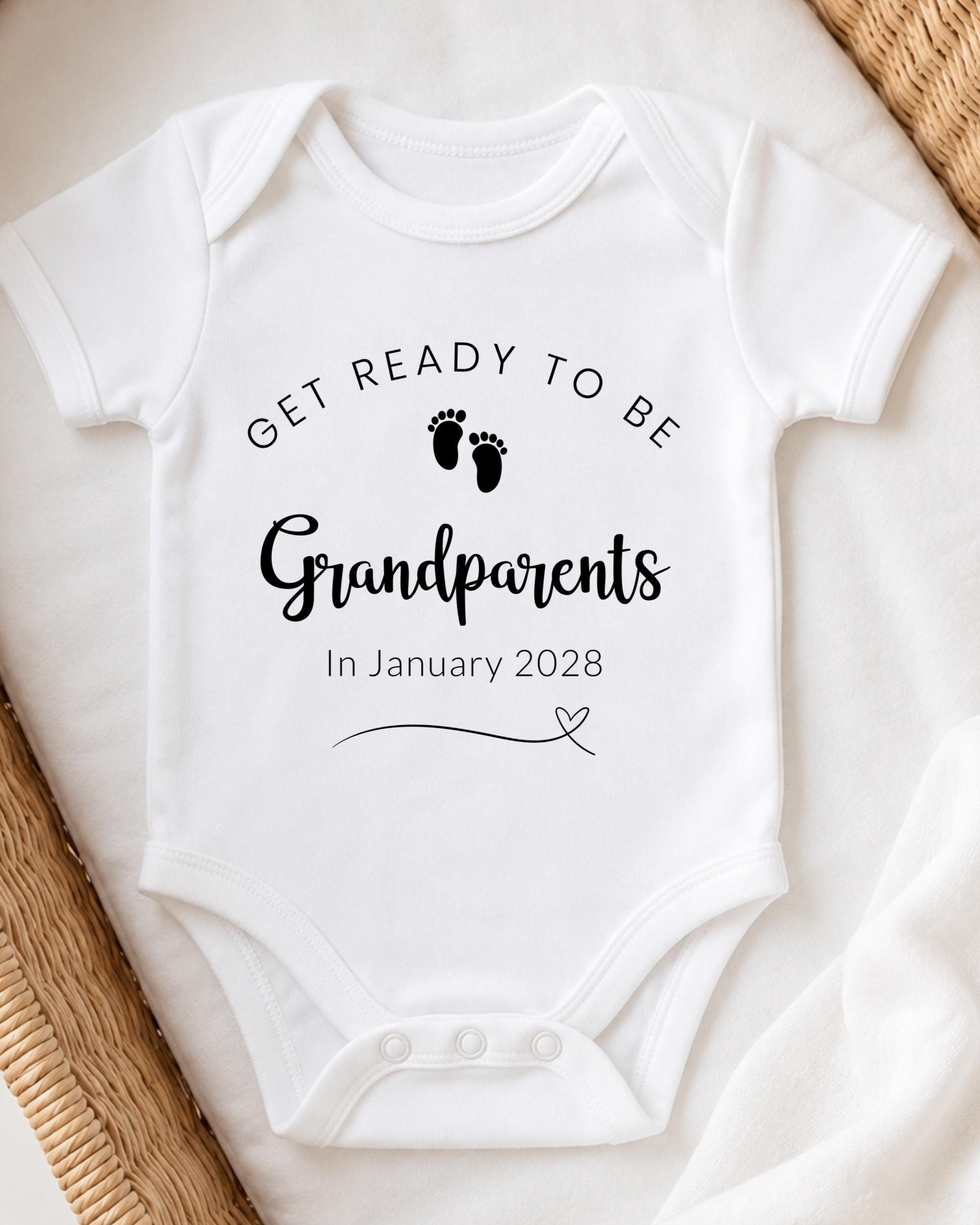 A white baby onesie with text and a graphic of baby footprints, placed on a white blanket.