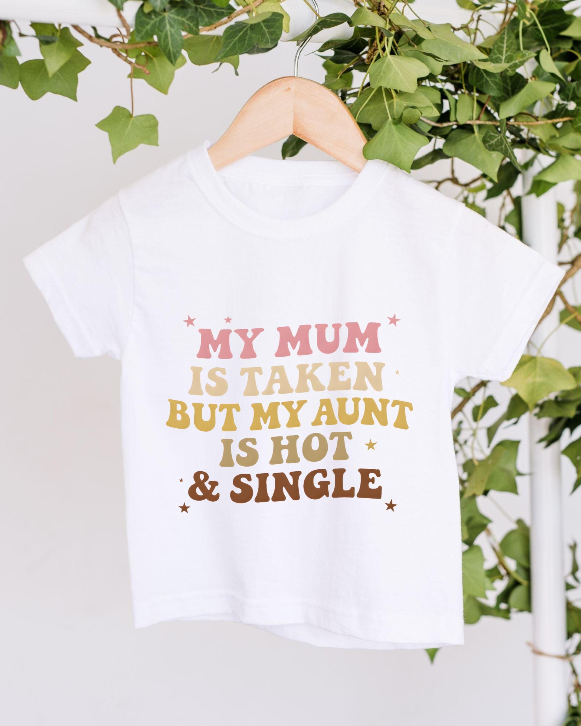 A white t-shirt with a humorous text printed on it, hanging on a wooden hanger.