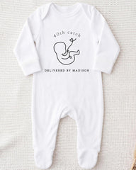 A white onesie with a graphic of a baby and text that reads "40th catch DELIVERED BY MADISON".