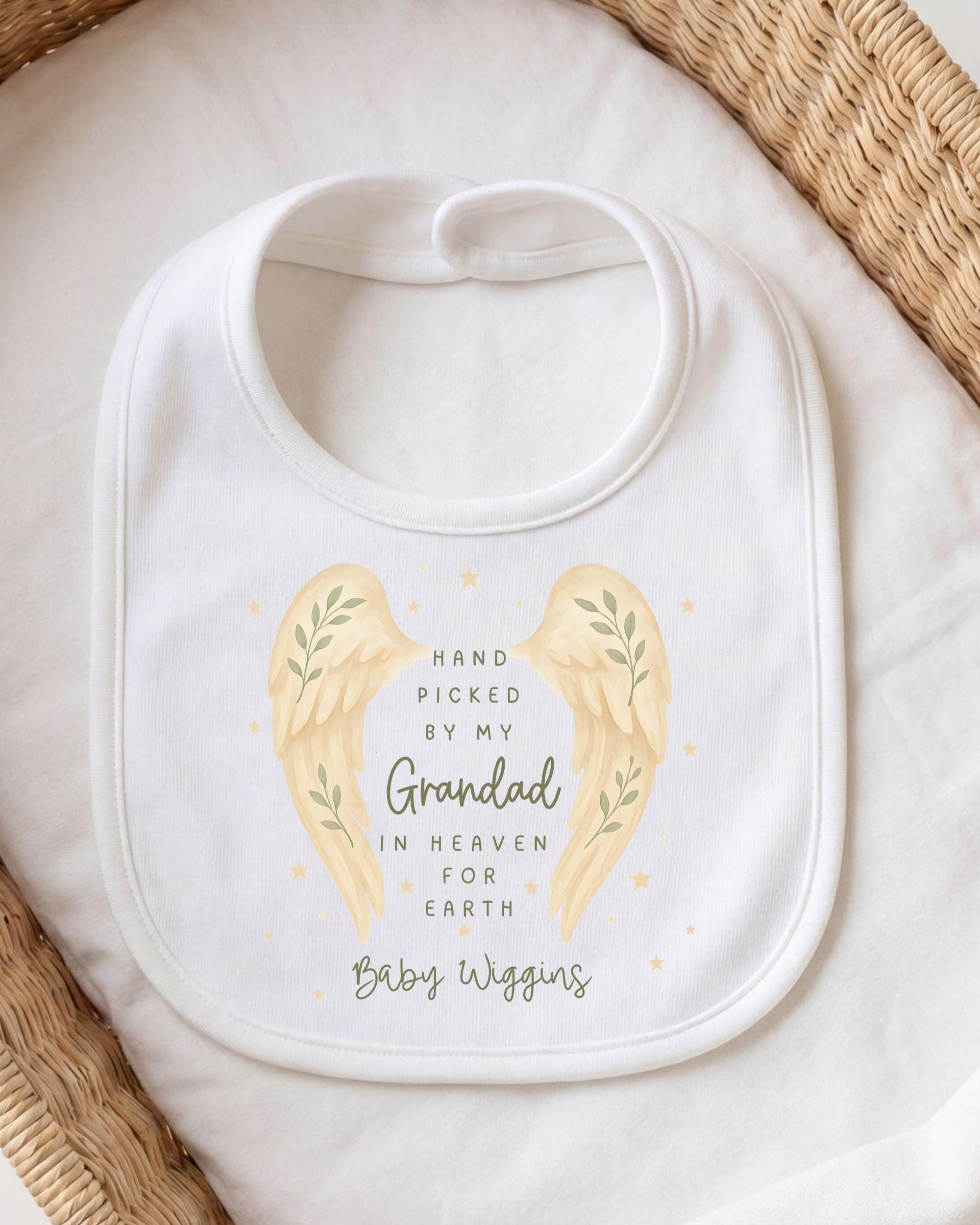 A white baby bib with a design featuring two angel wings and the text "Hand picked by my Grandfather in Heaven for Earth Baby Wiggins".