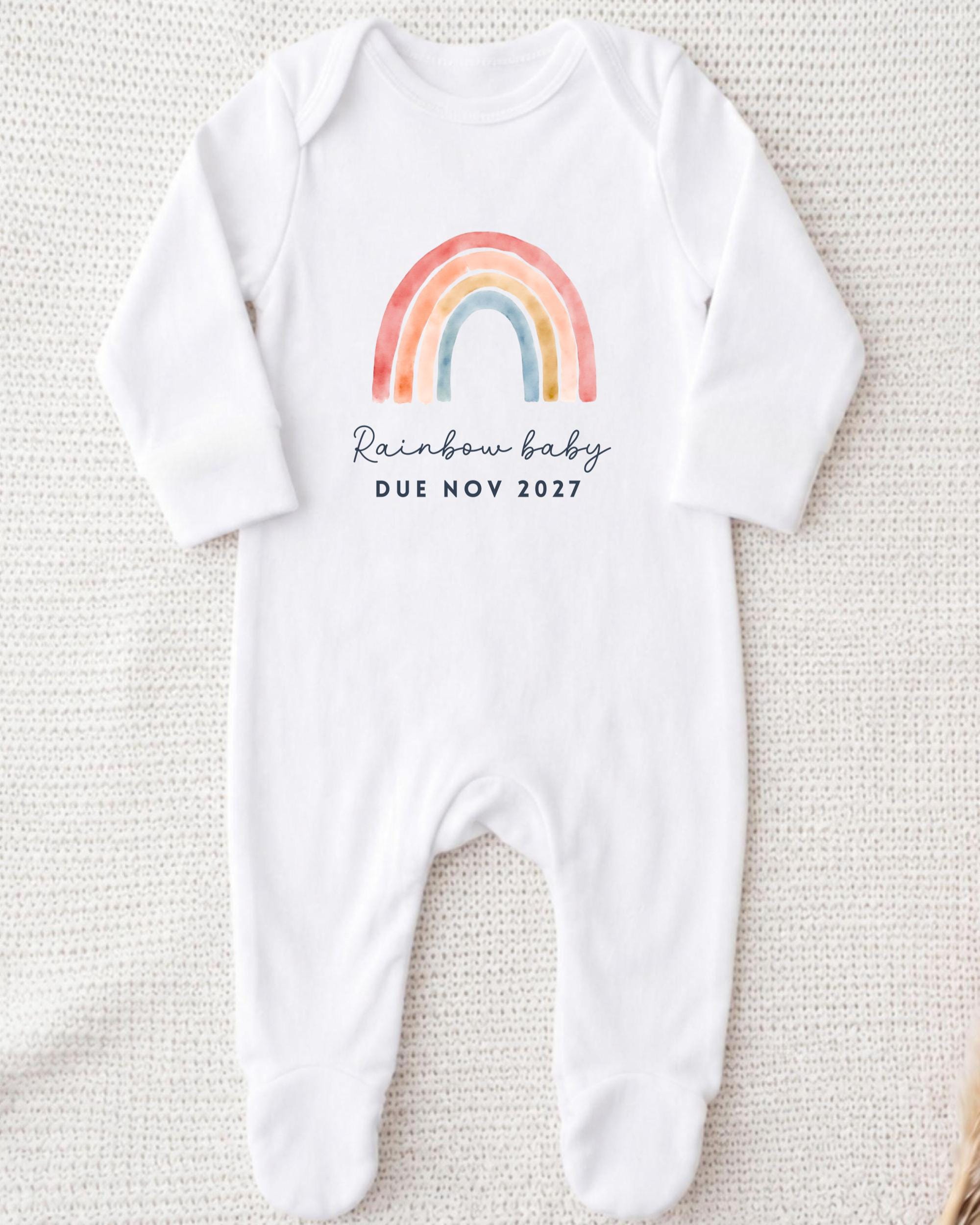 A white onesie with a rainbow graphic and the text "Rainbow baby due novely 2017" printed on it.