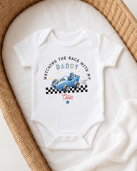 A white onesie with a racing car design and text printed on it, placed in a woven basket.