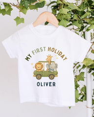 A white t-shirt with a graphic design featuring a lion, giraffe, and elephant in a safari vehicle, along with the text "My first holiday Oliver".
