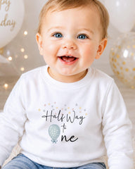 A smiling baby wearing a white shirt with the text "Half Way to One" printed on it.