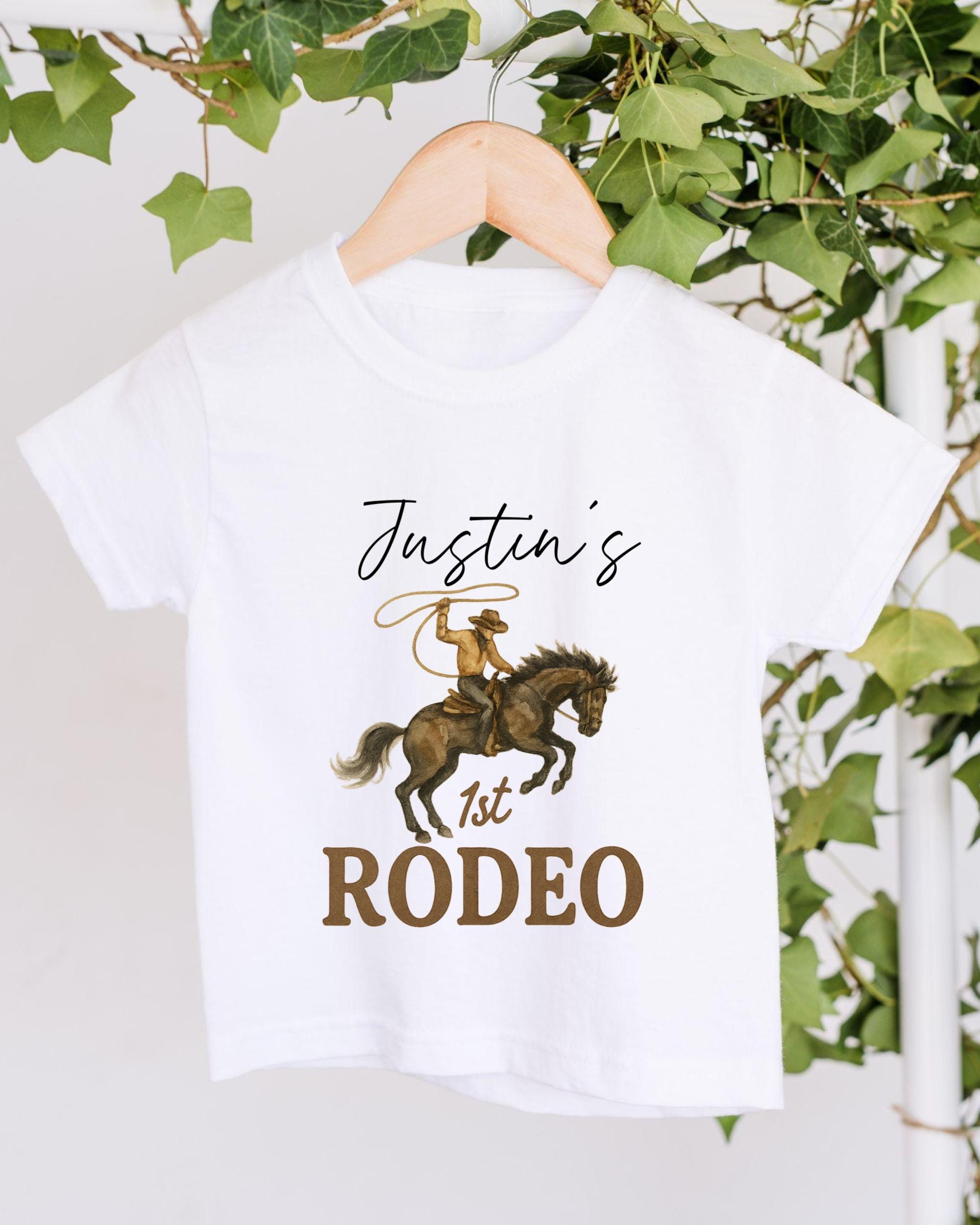 A white t-shirt with a cowboy riding a horse and the text "Justin's 1st Rodeo" printed on it.