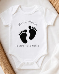 A white onesie with a black footprint design and text printed on it.