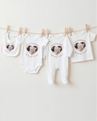 a collection of white baby clothes and bibs hanging on a clothesline, each featuring a heart-shaped design with a photograph of an elderly person.