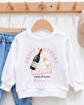 A white sweatshirt with a graphic design on it, featuring a bottle of wine and a baby bottle, along with the text "Happy Birthday Daddy Lots of Love Annex".