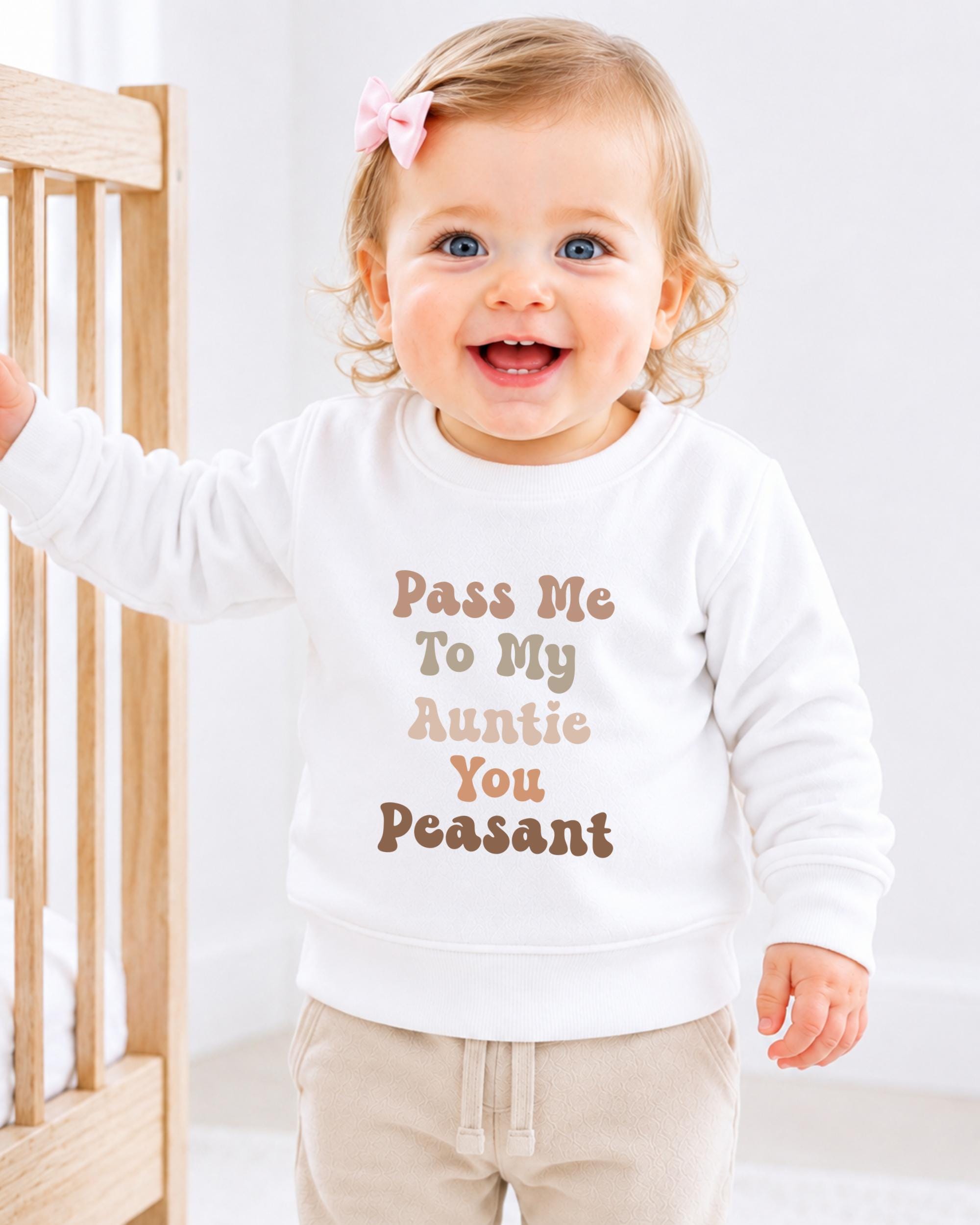 A smiling baby girl wearing a white sweater with text on it.