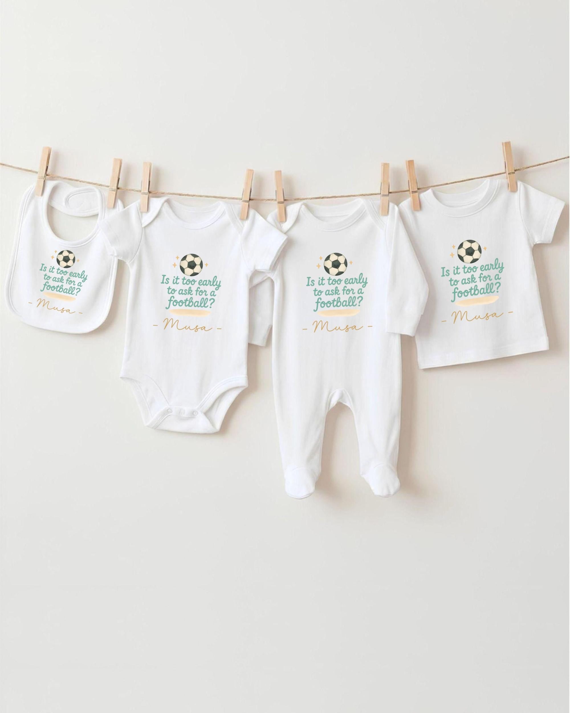 a collection of four white baby clothes hanging on a clothesline, with each piece featuring a soccer ball design.