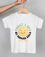 A white t-shirt with a yellow smiley face graphic and text printed on it.