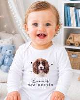 A smiling baby girl wearing a white onesie with a dog image and the text "Luna's New Bestie" printed on it.