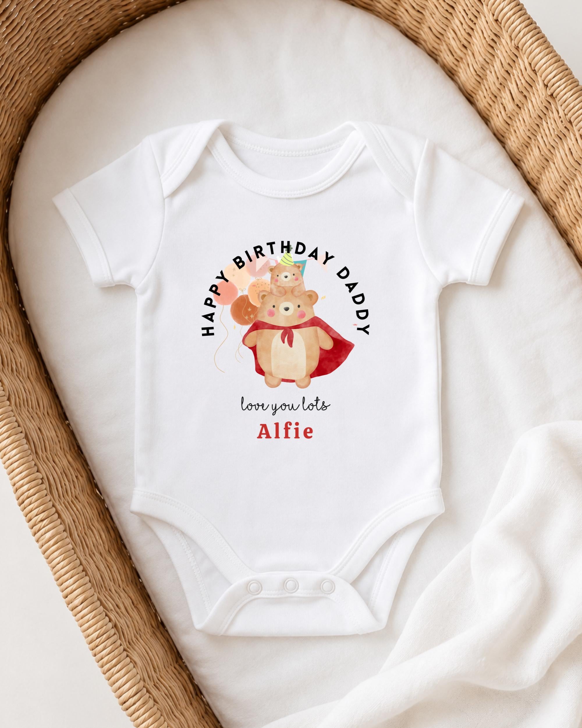 A white onesie with a graphic of a bear and the text "Happy Birthday Daddy" printed on it, placed on a white blanket.