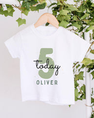 A white t-shirt with a green number 5 and the text "Today Oliver" printed on it, hanging on a wooden hanger.
