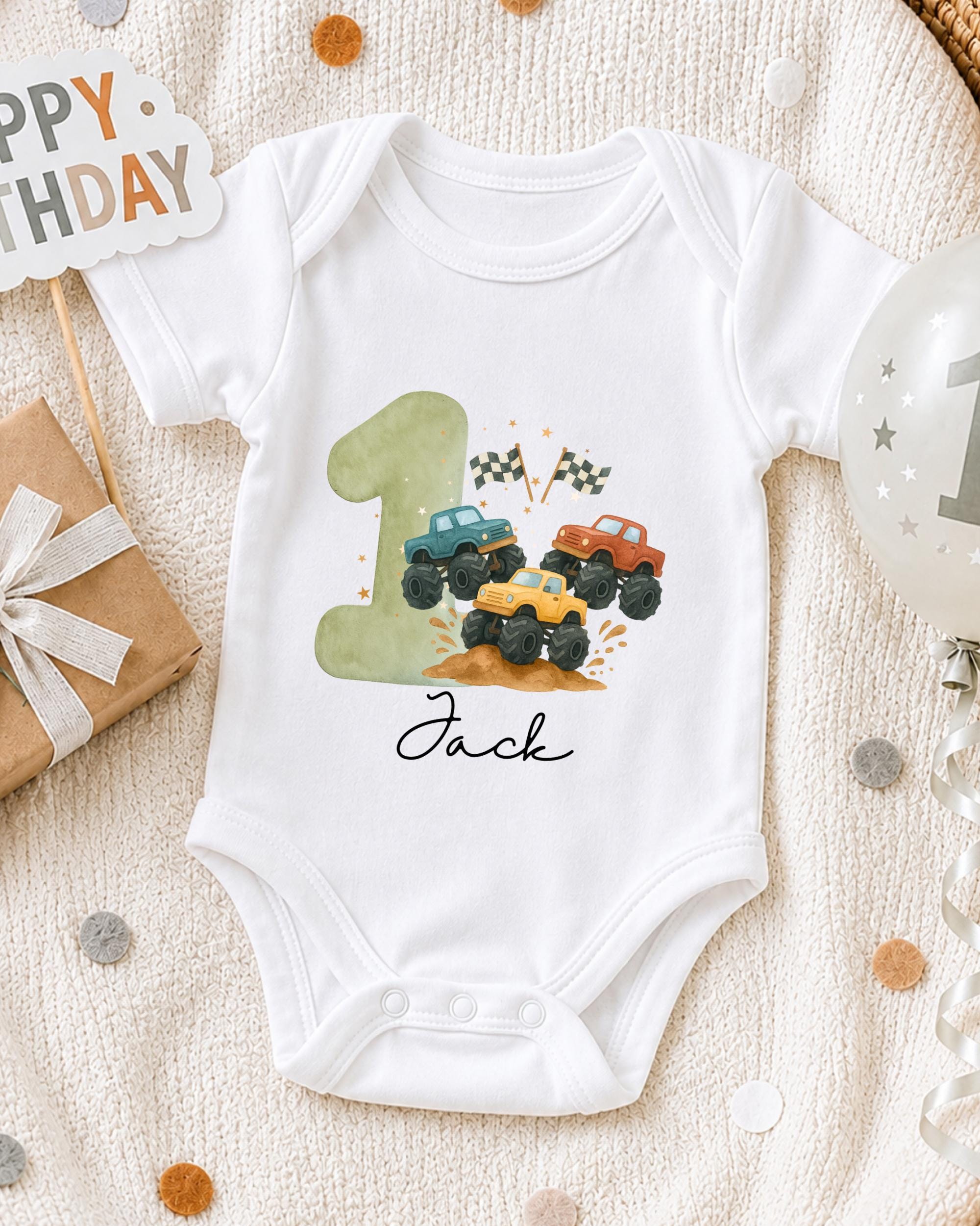A white onesie with a graphic of a truck on it, along with a birthday sign and a balloon, all placed on a white blanket.