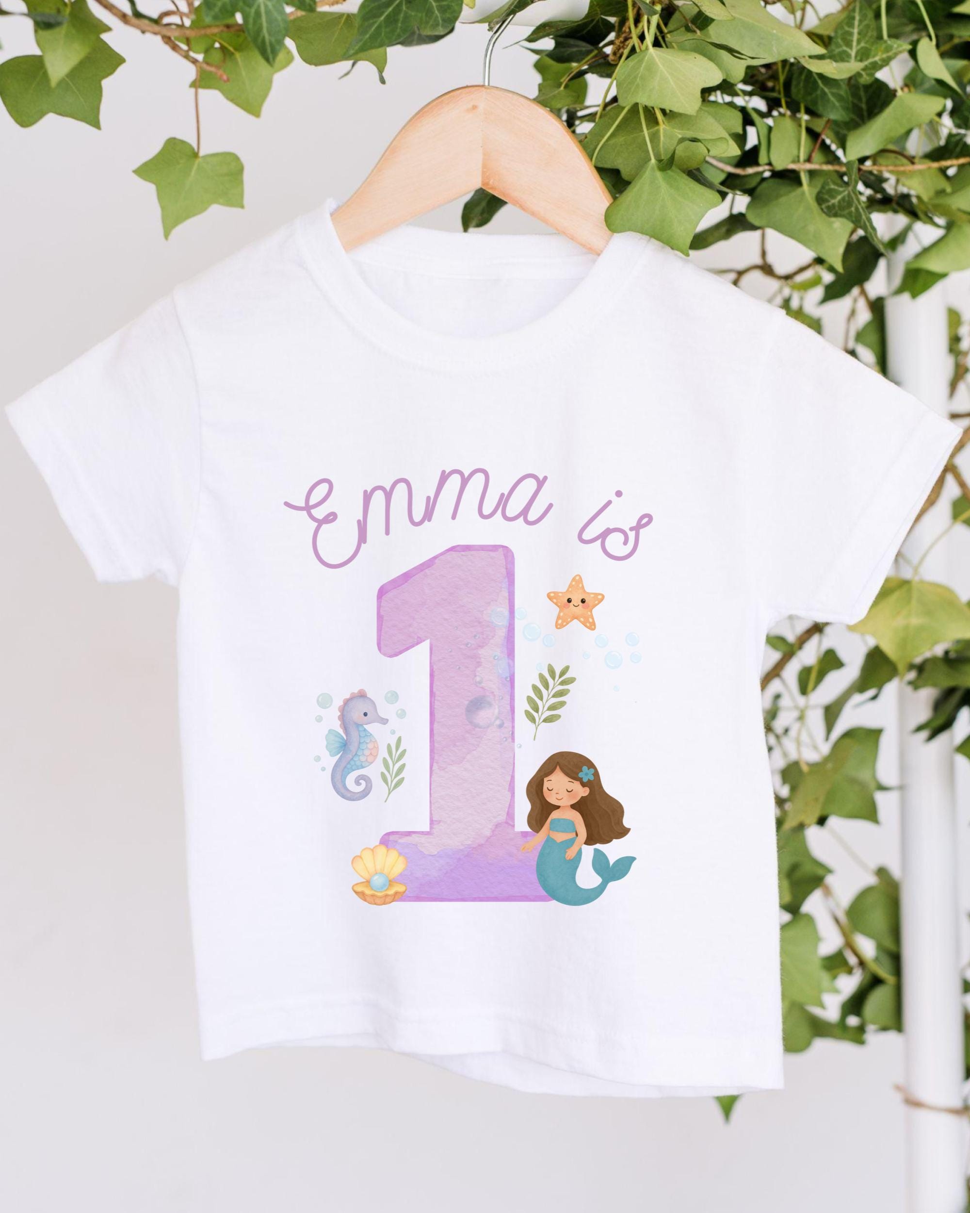 A white t-shirt with a mermaid and a number 1 printed on it, along with some marine-themed elements.