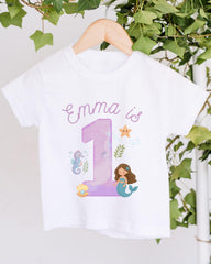 A white t-shirt with a mermaid and a number 1 printed on it, along with some marine-themed elements.