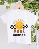 A white t-shirt with a cheerful smiley face and text printed on it, hanging on a wooden hanger.