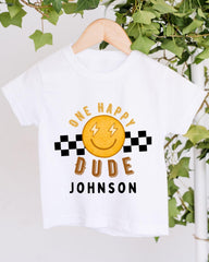 A white t-shirt with a cheerful smiley face and text printed on it, hanging on a wooden hanger.