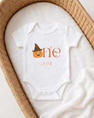 A white onesie with a pumpkin and a witch hat on it, placed in a wicker basket.