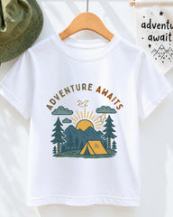 A white t-shirt with a graphic design depicting a camping scene with mountains, pine trees, and a tent, along with the text "Adventure Awaits" printed on it.