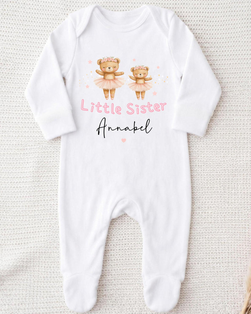 A white bodysuit with a design of two teddy bears in tutus and the text "Little Sister Annabel" printed on it.