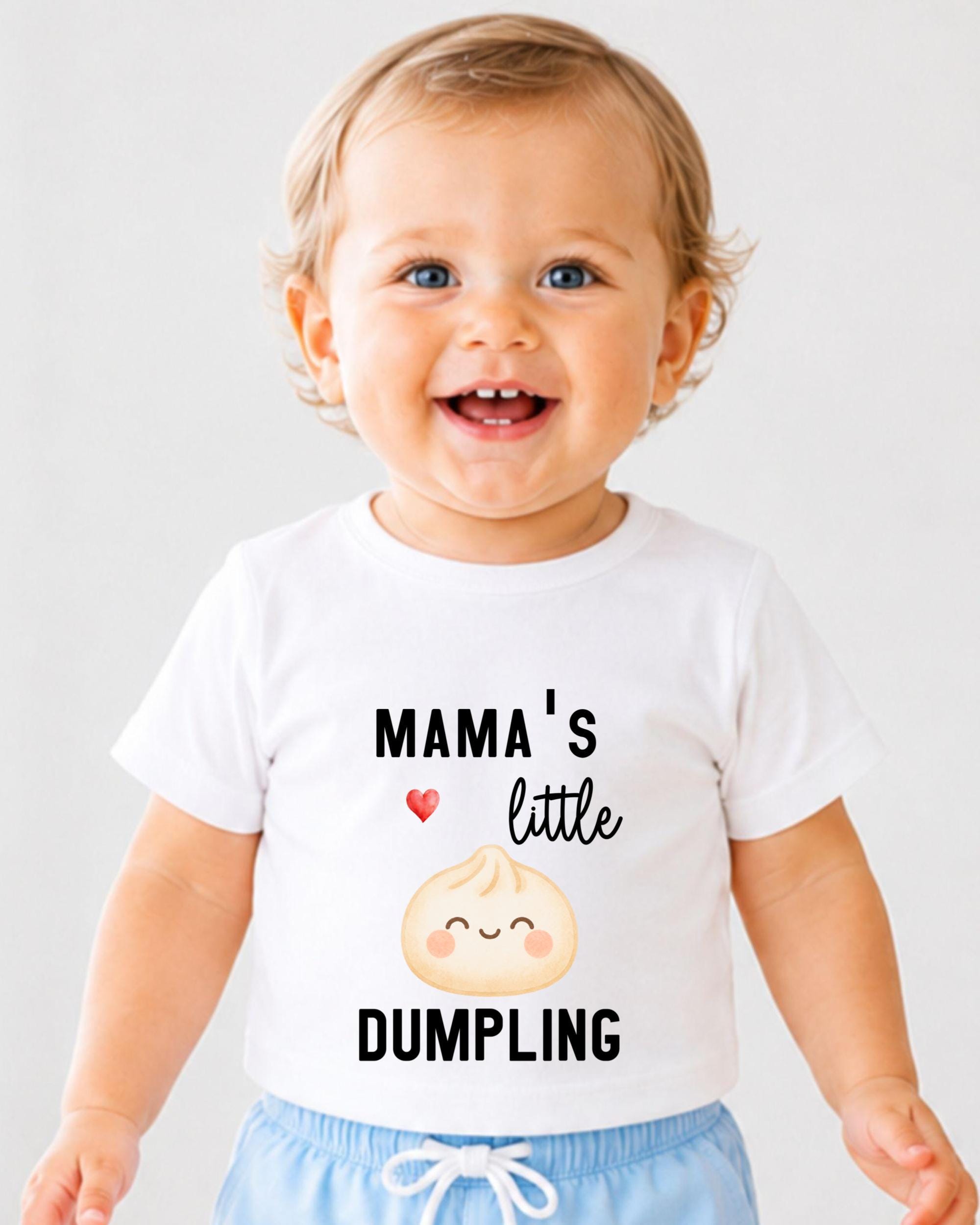 A smiling baby wearing a white t-shirt with a printed design and text.