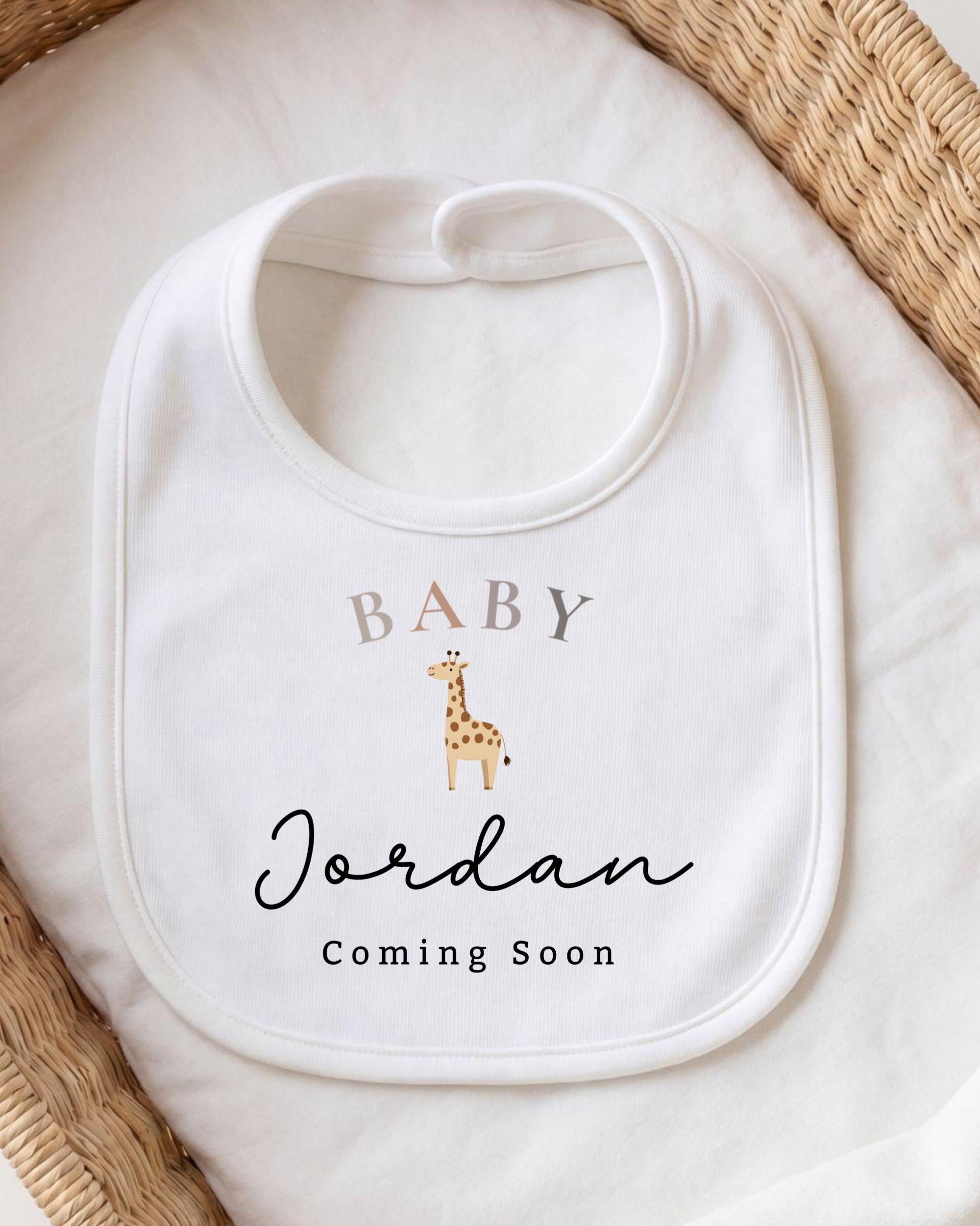 A white baby bib with a giraffe design and the text "BABY Jordan Coming Soon" printed on it.