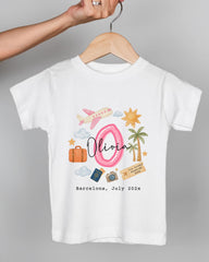 A white t-shirt with a graphic design featuring a pink number 8, a pink airplane, a suitcase, a palm tree, and various travel-related icons. The text below the design reads "Olivia Barcelona July 2023".