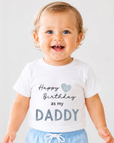 A smiling baby wearing a white t-shirt with text that says "Happy 1st Birthday as my DADDY".