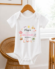 A white baby onesie with a printed design on it, hanging on a wooden hanger.