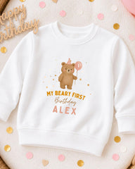 A white sweatshirt with a cartoon bear and the text "My Beary First Birthday Alex" printed on it, along with a birthday balloon.