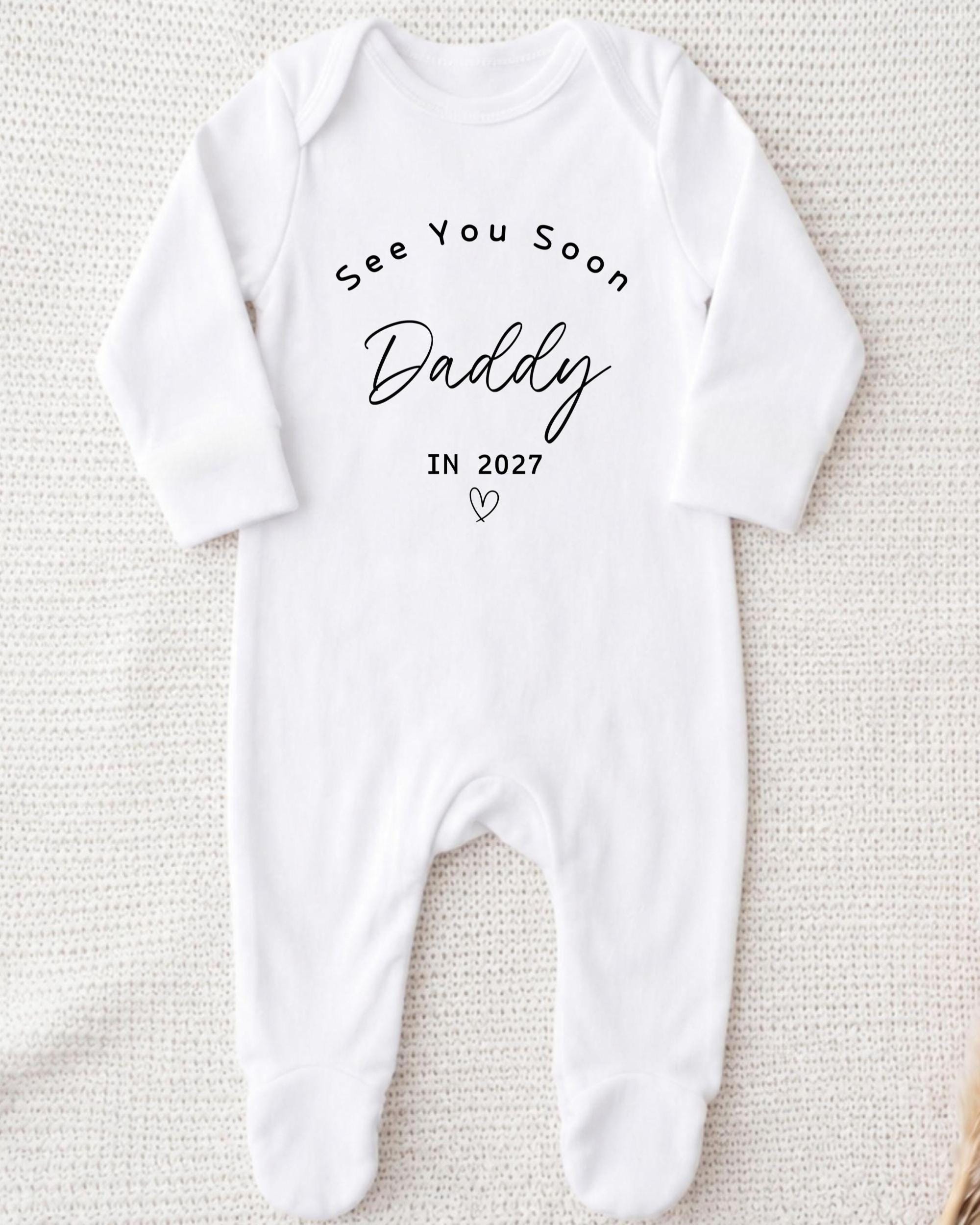 A white onesie with the text "See You Soon Daddy" printed on it.