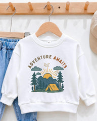 A white sweatshirt with a graphic design of a camping scene and the text "Adventure Awaits" printed on it, hanging on a wooden hanger.
